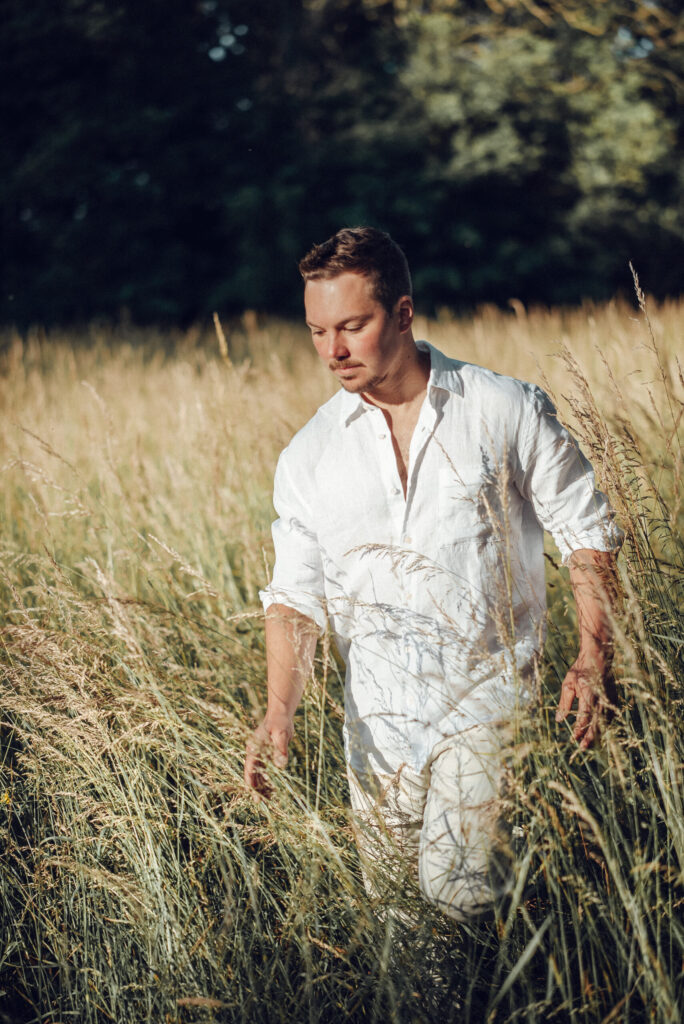 Tim Böttner im weißen Hemd geht durch hohes Gras