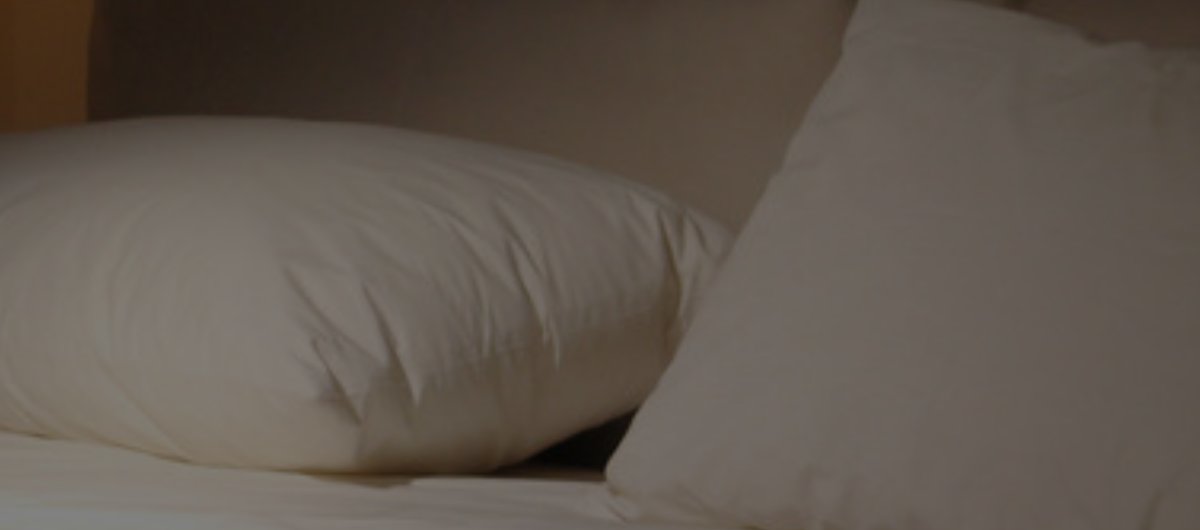 Ruhiges, abgedunkeltes Schlafzimmer mit weißem Bettzeug und Kissen