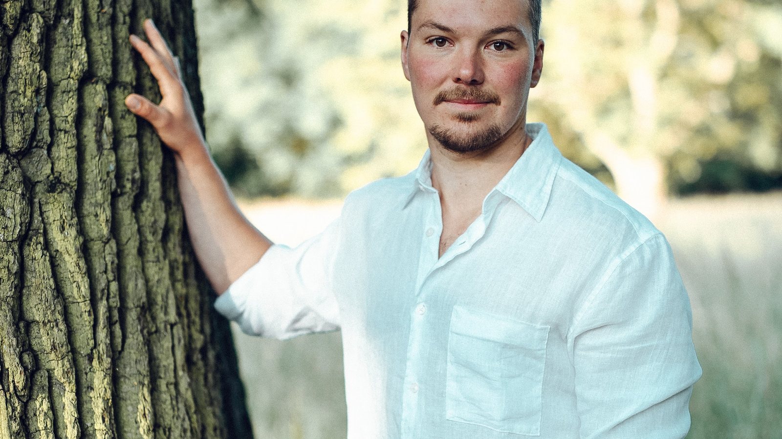 Tim lehnt mit einer Hand an einem großen Baum